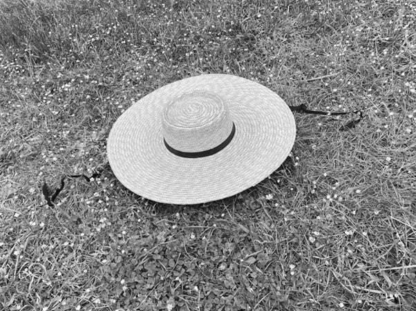 wide brimmed straw hat lay on grass with black ribbon trailing